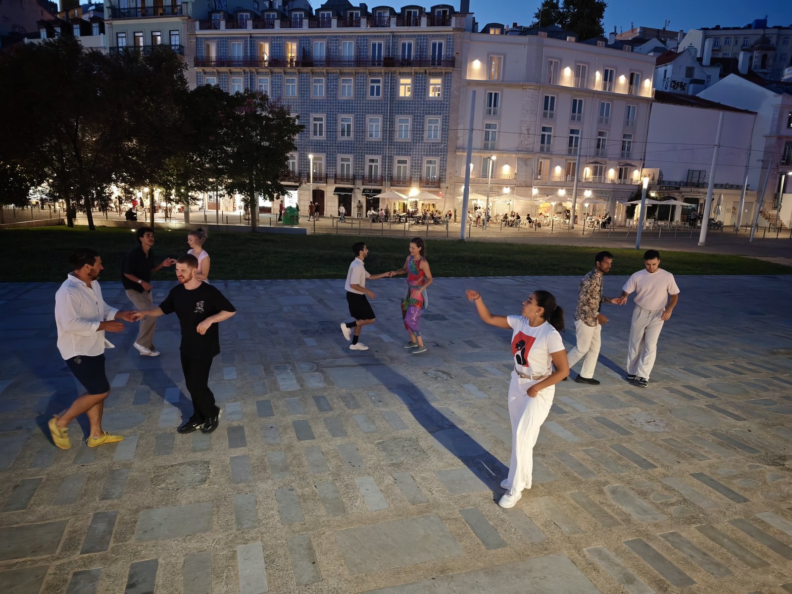 Pessoas a praticar a pares numa praça de Lisboa, ao anoitecer